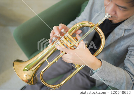 Asian man plays cornet. A solo Asian skillful musician is playing or practicing cornet in the restaurant. A man enjoy playing cornet or trumpet. Asian man plays cornet. A solo Asian skillful musician is playing or practicing cornet in the restaurant. A man enjoy playing cornet or trumpet. 120948633