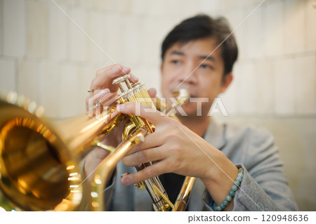 Asian man plays cornet. A solo Asian skillful musician is playing or practicing cornet in the restaurant. A man enjoy playing cornet or trumpet. 120948636