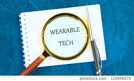 WEARABLE TECH concept word in a clean notebook through a magnifying glass 120948878