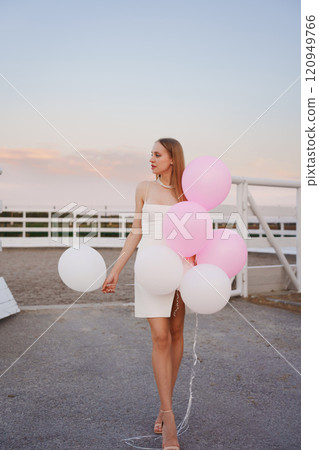 Beautiful slender blonde with long hair and balloons in an evening park. 120949766