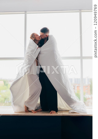 A gentle and romantic man and woman wrapped in a blanket on the windowsill A gentle and romantic man and woman wrapped in a blanket on the windowsill 120949769