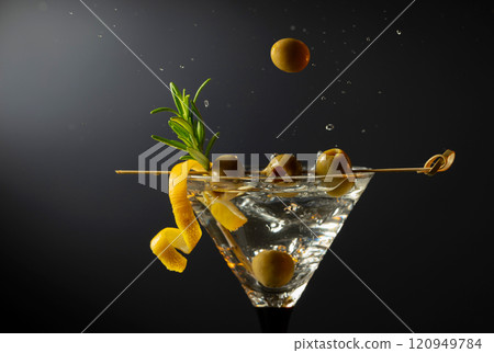 Classic dry martini cocktail with green olives, lemon peel, and rosemary on a black background. Classic dry martini cocktail with green olives, lemon peel, and rosemary on a black background. 120949784