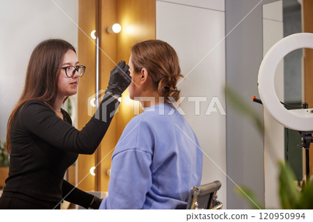Eyebrow Expert, Professional Microblading, Salon Procedure. Woman is at beauty salon, undergoing sophisticated eyebrow correction procedure that includes microblading and smudge repair. Eyebrow Expert, Professional Microblading, Salon Procedure. Woman is at beauty salon, undergoing sophisticated eyebrow correction procedure that includes microblading and smudge repair. 120950994