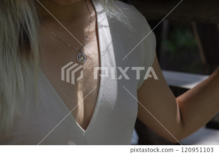 Women dressed cream v-neck shirt showing cleavage with necklace and morning sun. 120951103
