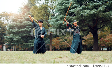Sword, martial arts and people in outdoor training together for aikido, fight coaching or samurai challenge in nature. Warrior, Japanese man and woman in park for traditional bokken battle with wood Sword, martial arts and people in outdoor training together for aikido, fight coaching or samurai challenge in nature. Warrior, Japanese man and woman in park for traditional bokken battle with wood 120951127