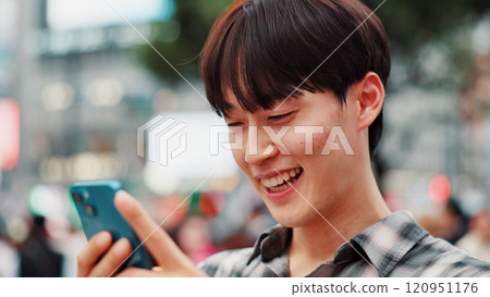 Man, phone and happy with travel in city, reading and check notification with chat, laugh or meme in street. Person, smartphone and outdoor on metro sidewalk, smile and app for social media in Japan 120951176