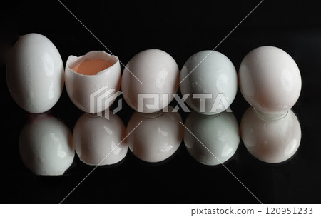 The reflection of Five raw duck eggs are sitting in a row with an egg broken in half showing the yolk and white egg on black background. 120951233