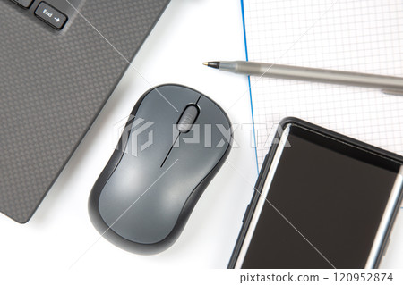 Computer wireless mouse, pen and notepad next to a laptop on a white table close-up Computer wireless mouse, pen and notepad next to a laptop on a white table close-up 120952874