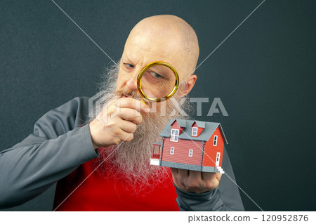 bearded man examines a miniature model of a residential building through a magnifying glass bearded man examines a miniature model of a residential building through a magnifying glass 120952876