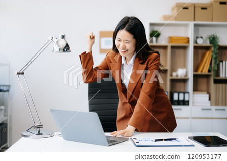 Asian business woman are delighted and happy with the work they do on their tablet, laptop and taking notes 120953177