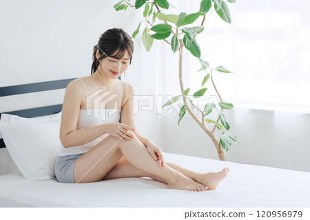 Woman doing skin care for legs in bed Woman doing skin care for legs in bed 120956979