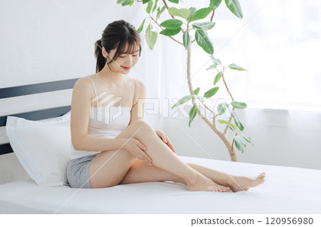 Woman doing skin care for legs in bed Woman doing skin care for legs in bed 120956980