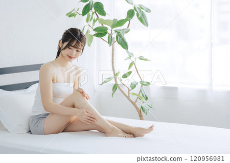 Woman doing skin care for legs in bed Woman doing skin care for legs in bed 120956981