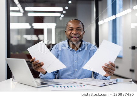 Mature african american businessman smiling confidently, holding papers in a modern office setting. Represents success, positivity, and professionalism in workplace environment. Mature african american businessman smiling confidently, holding papers in a modern office setting. Represents success, positivity, and professionalism in workplace environment. 120957480