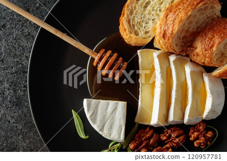 Camembert cream cheese with honey, croissants, and walnuts on a black plate. 120957781