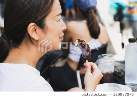 Middle aged woman enjoy eating frozen banana with chocolate on a Stick. 120957876