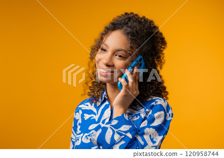 Attractive young adult african woman talking by phone, smiling. Young lady on yellow background. Teenager girl having smartphone call. 120958744