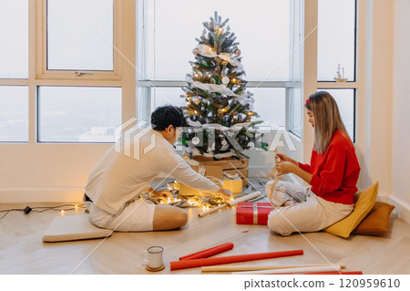 Husband and wife couple lover decorating Christmas tree together while man setting up the tree and woman packing the box. 120959610
