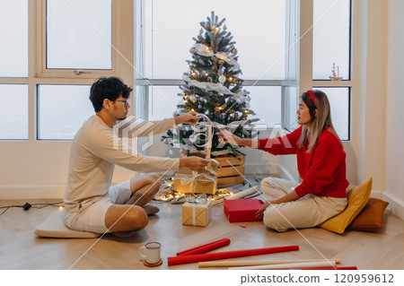 Husband and wife couple lover decorating Christmas tree together while the man helping woman packing decoration boxes. Husband and wife couple lover decorating Christmas tree together while the man helping woman packing decoration boxes. 120959612