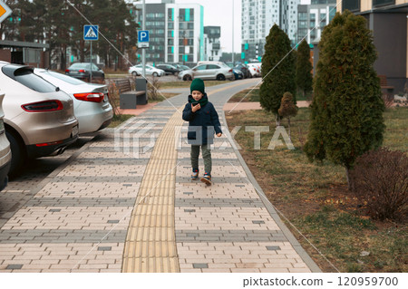 Child walking on a sidewalk in a modern urban area while using a smartphone Child walking on a sidewalk in a modern urban area while using a smartphone 120959700