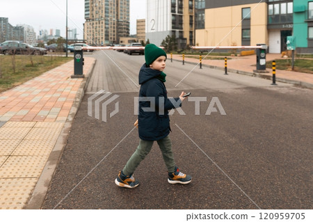 Young boy crossing a suburban street in a modern neighborhood during daylight hours while holding a Young boy crossing a suburban street in a modern neighborhood during daylight hours while holding a 120959705