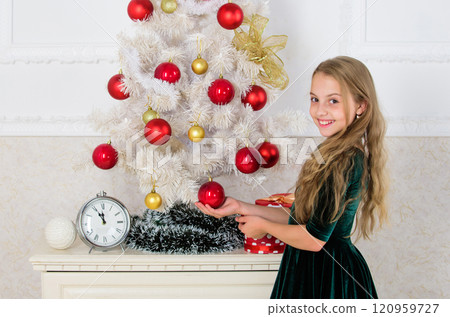 Girl celebrate christmas. Child put christmas ornament ball on artificial white tree. Top christmas decorating ideas for kids room. Kids can brighten up christmas tree by creating their own ornaments 120959727