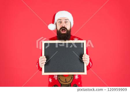 Unbelievable. Winter announcement. Winter event. Winter holidays. Man hold blank blackboard copy space. Guy santa claus red background. Santa Claus hat with advertisement. Chalkboard for information 120959909