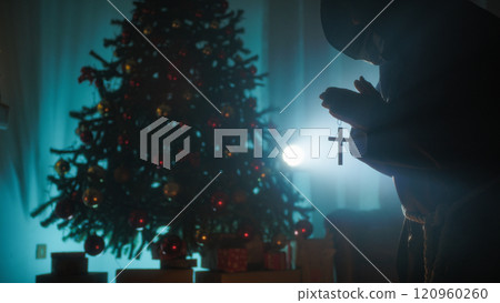Man Prays With Crucifix In Front Of Christmas Tree In Silhouette Man Prays With Crucifix In Front Of Christmas Tree In Silhouette 120960260