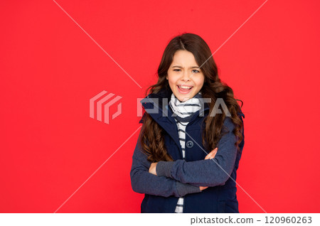 emotional kid with curly hair in puffer waistcoat. teen girl on red background. portrait of child 120960263