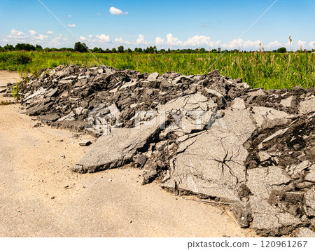 Asphalt remnants by a rural path create a picturesque scene under a clear blue sky with lush greenery 120961267
