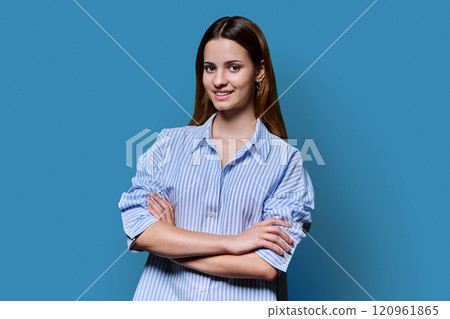 Beautiful young girl with crossed arms looking at camera on blue background 120961865
