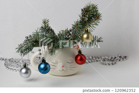 The branches of the Christmas tree decorated toys, are placed in a cute white cup in the shape of a sleeping cat's head. 120962352