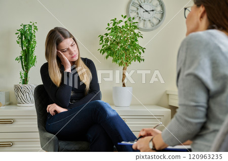 Sad unhappy young woman at therapy with female professional mental specialist 120963235