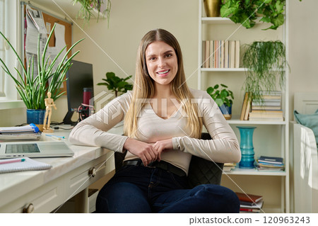 Portrait of young smiling beautiful woman looking at camera sitting at home at desk Portrait of young smiling beautiful woman looking at camera sitting at home at desk 120963243