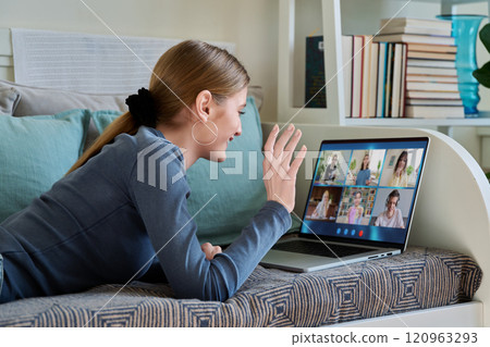 Female teenage student having group video conference, using digital tablet, lying on couch at home. Female teenage student having group video conference, using digital tablet, lying on couch at home. 120963293