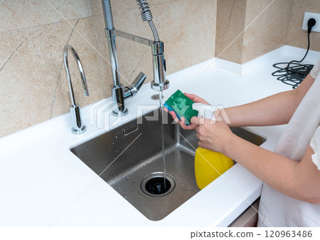 Washing dishes with a sponge and soap under running water in a modern kitchen sink. 120963486