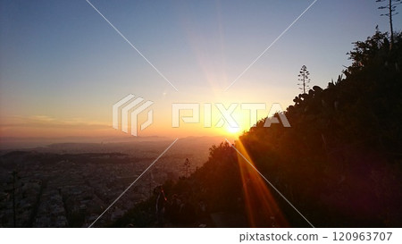 Athens, Greece - 30.3.2018: The sun falling behind the hillside of Lykavittos Hill with the urban skyline with Panathenaic Stadium in sight and the Aegean Sea at the horizon during sunset in spring 120963707
