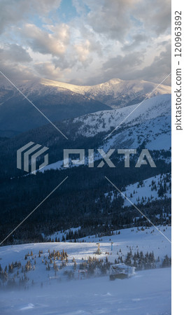 Alpine resortr ski lift with seats going over the sunset mountain skiing  slopes in extremally windy weather 120963892