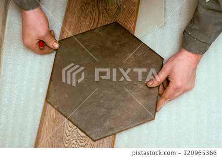 Hands are artistically arranging a hexagonal tile on a soft surface, blending textures and colors in an interior space. The focus is on the craftsmanship and attention to detail in the renovation. 120965366