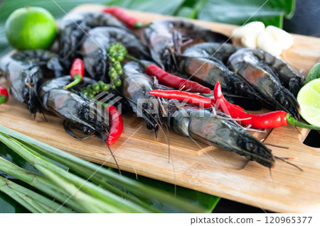 A vibrant display of freshly caught tiger shrimp arranged with fresh herbs, chili peppers, and lime on banana leaves evokes the rich flavors of Asian cuisine, showcasing a culinary tradition. 120965377