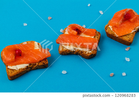 Fresh delicious croutons with salmon on a blue background, sprinkled with salt Fresh delicious croutons with salmon on a blue background, sprinkled with salt 120968283
