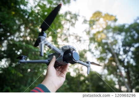 Drone with camera in hand before flying, bokeh background in green forest. 120968296