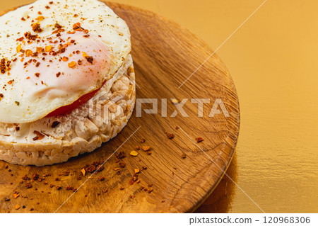 Egg on rice bread with tomato, cheese on a wooden plate on a golden background Egg on rice bread with tomato, cheese on a wooden plate on a golden background 120968306