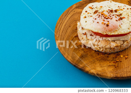 Egg on rice bread with tomato and cheese on a wooden plate on a blue background 120968333