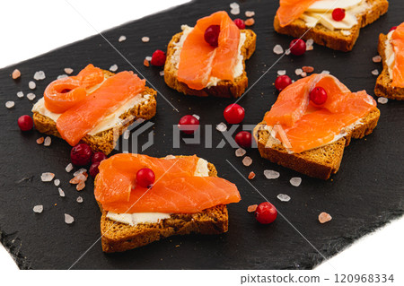 Toasts with butter salmon and cranberries on a stone board on a white background 120968334