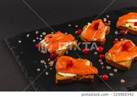 Toasts with butter, mozzarella and salmon on a stone board on a black background Toasts with butter, mozzarella and salmon on a stone board on a black background 120968342