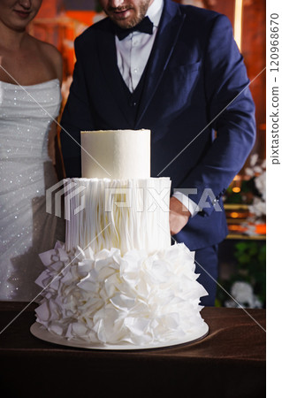 The bride and groom stand next to a wedding cake. 120968670