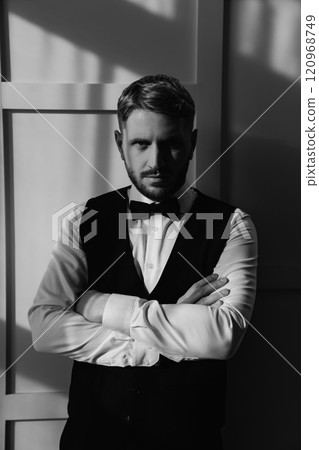 The groom in a waistcoat and tie bow against a white wall. black and white The groom in a waistcoat and tie bow against a white wall. black and white 120968749