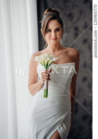 bride in a tight-fitting dress with a bouquet calla by windows in a hotel room. bride in a tight-fitting dress with a bouquet calla by windows in a hotel room. 120968770