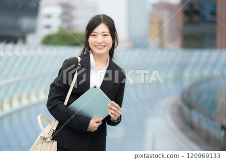 A businesswoman wearing a suit and holding a tablet in an office district 120969133